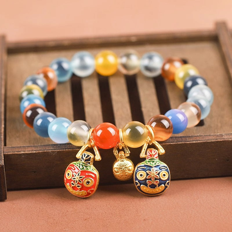Multi-colored candy agate bead bracelet with gold-tone charms on a wooden tray