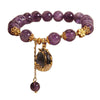 Purple amethyst beaded bracelet with a gold-tone lily flower charm resting on a box.