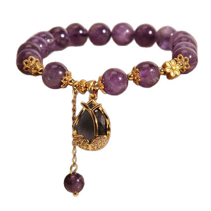 Purple amethyst beaded bracelet with a gold-tone lily flower charm resting on a box.