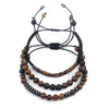 Three layered bracelets featuring tiger eye beads and black braided cords on a stone surface