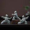 Three grey geometric Tai Chi figures in different poses on a dark wooden surface