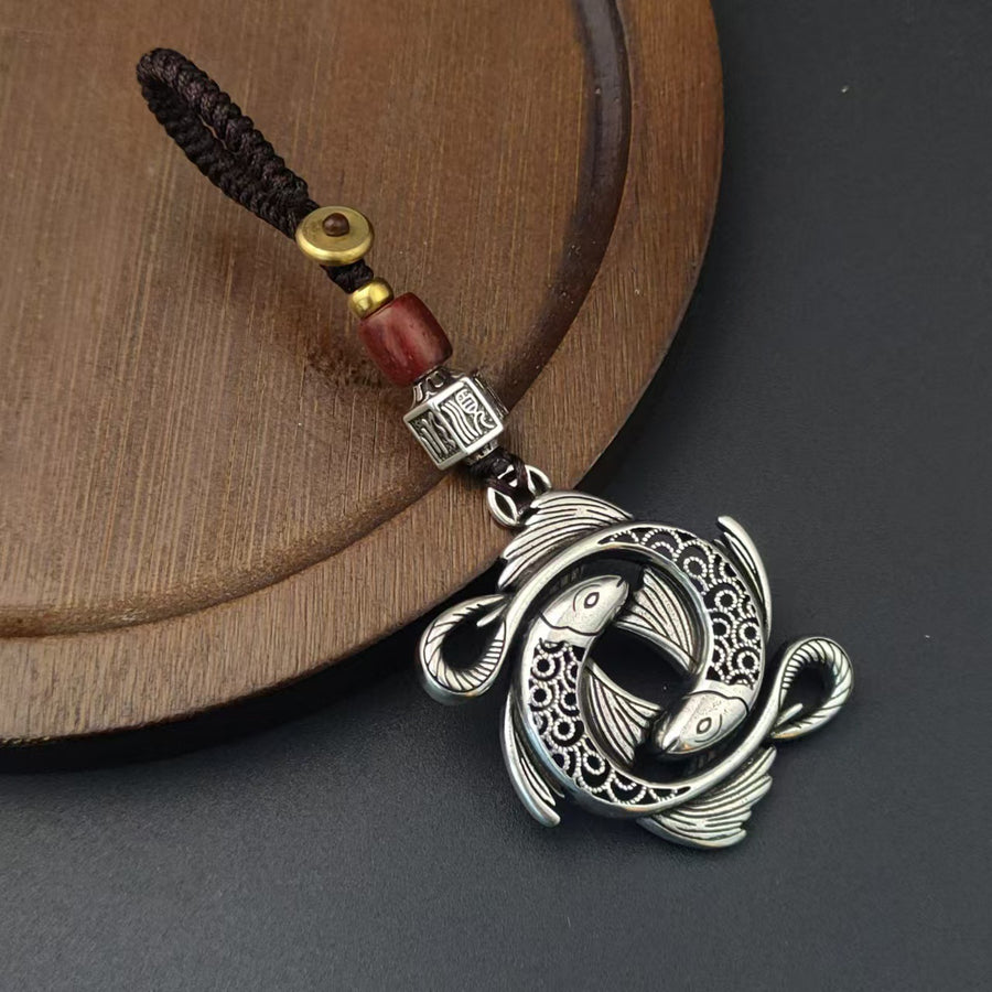 Close up of a vintage copper keychain with a double koi fish charm on a wooden surface.