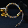 Close up of a multicolored braided rope bracelet with gold beads and a bell