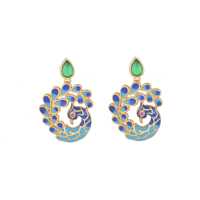 Pair of gold-tone peacock earrings with blue enamel and green agate stones on a wooden surface