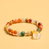 Close up of a multi-colored golden silk jade beaded bracelet with a white donut shaped pendant on a yellow background
