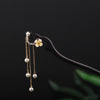 Close-up of a dark wooden hairpin with a white flower and hanging pearl chains on a black background.