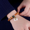 Hand holding a sandalwood bead bracelet with a white jade elephant pendant