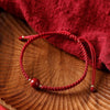 A red braided bracelet with a round red cinnabar bead resting on a wooden surface.