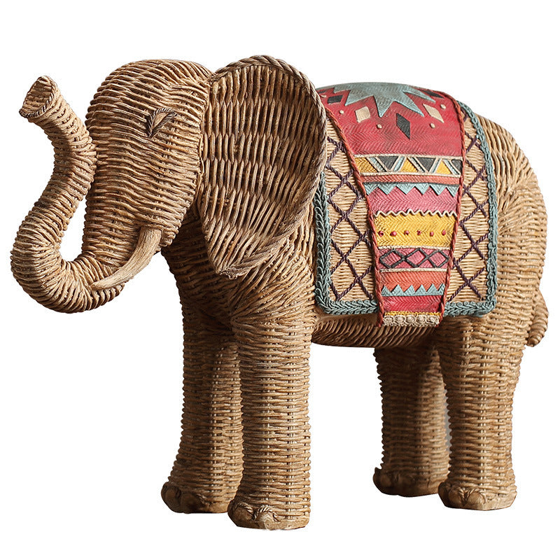 Two resin elephant statues with a woven texture and colorful blankets on a wooden table.