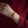 Close up of a red and multicolor braided bracelet with gold beads on a wrist