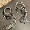 Two styles of black and white braided rope bracelets with Yin Yang and coin charms on a grey surface.