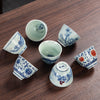 A collection of small white ceramic teacups with blue and red painted designs on a wooden table