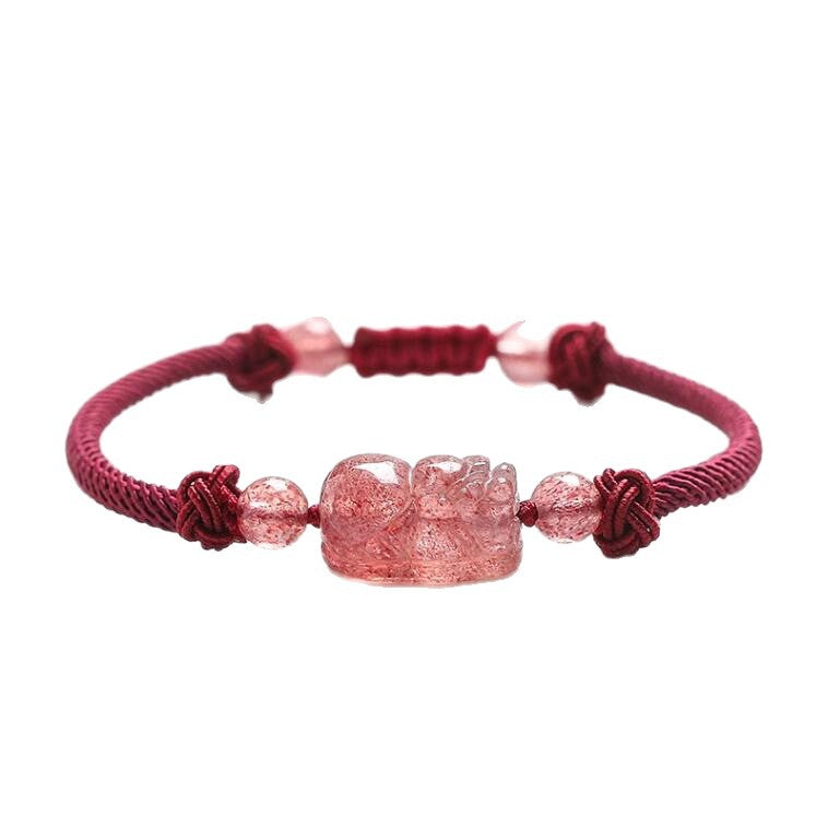 Hand wearing a red braided bracelet with a pink carved Pixiu charm