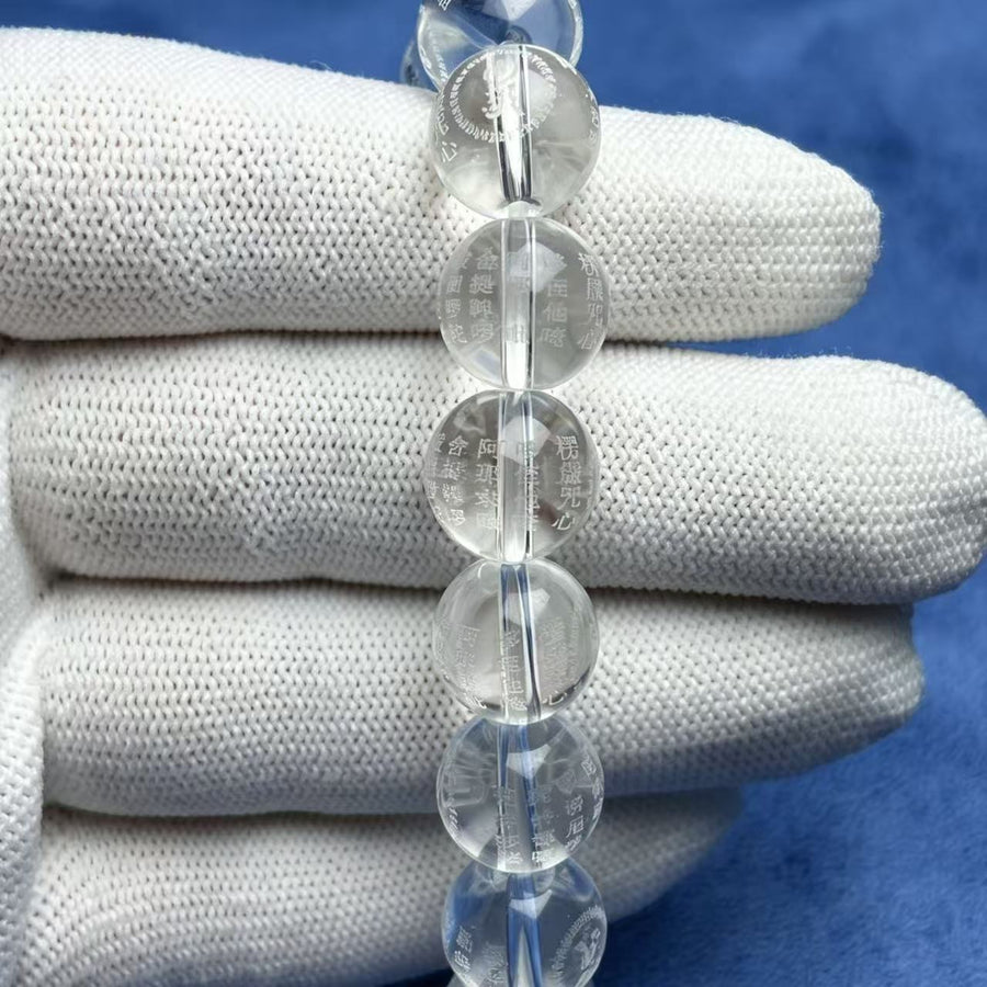 Close up of a clear glass bead bracelet held in a gloved hand showing internal engravings