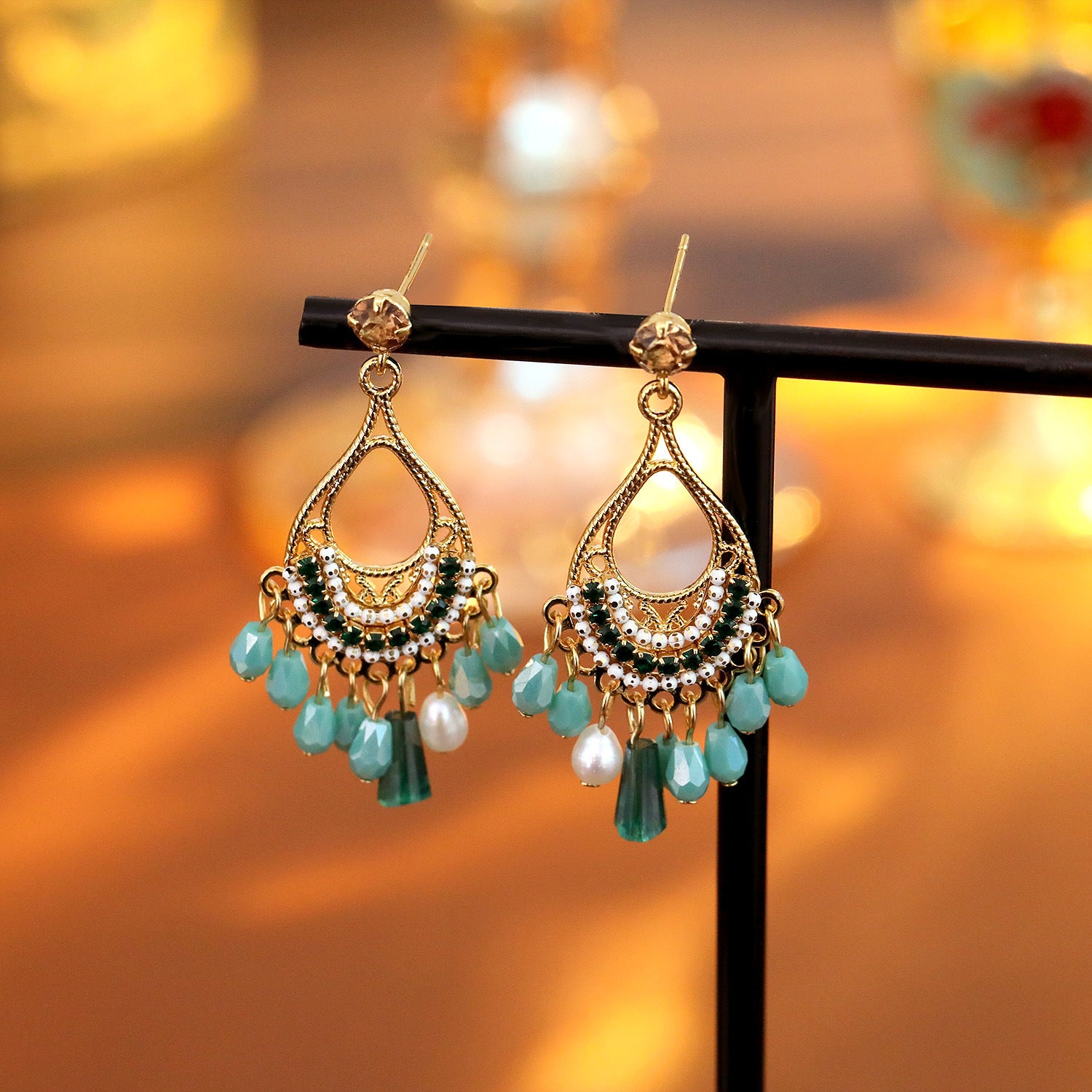Pair of gold-tone copper earrings with green beads and white pearls on a black stand