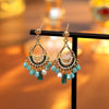 Pair of gold-tone copper earrings with green beads and white pearls on a black stand