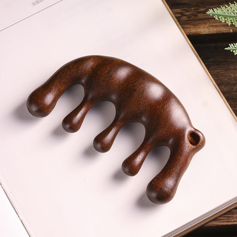 Dark brown wooden massage comb with five rounded prongs resting on a white book page