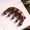 Dark brown wooden massage comb with five rounded prongs resting on a white book page