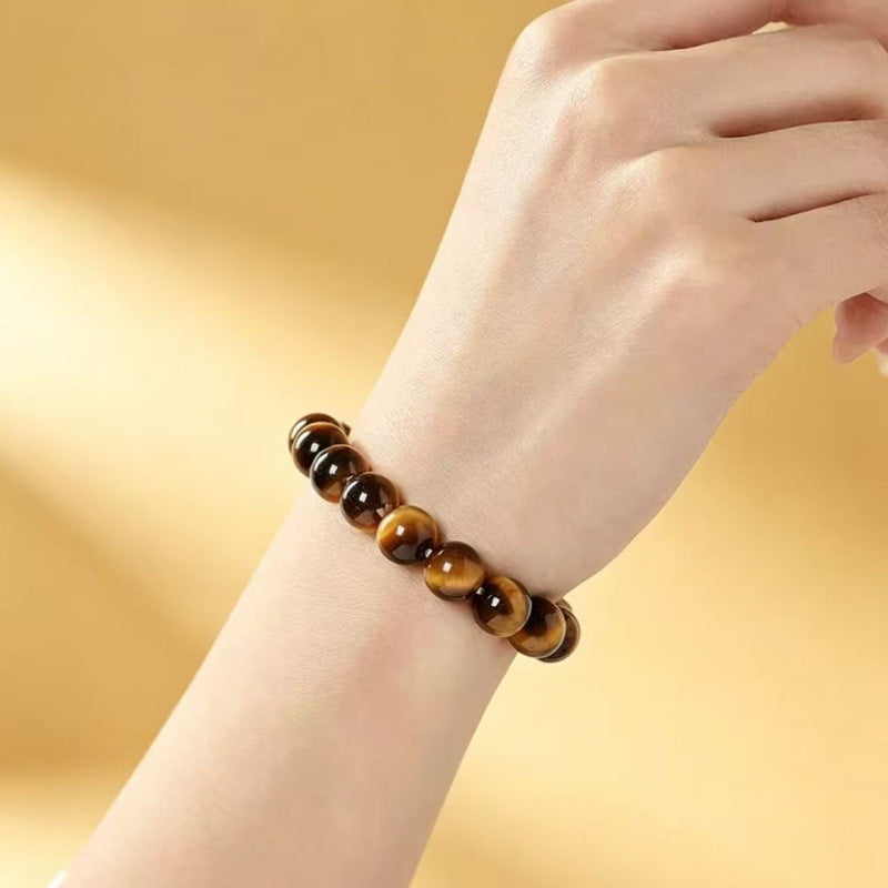 A wrist wearing a brown and gold natural tiger eye bead bracelet against a soft background
