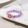 Close-up of a purple beaded ring with a pink enamel flower charm on a white surface