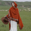 Woman wearing an orange hooded shawl with floral trim in a field