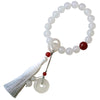 Hand holding a white agate wrist mala with red bead and tassel