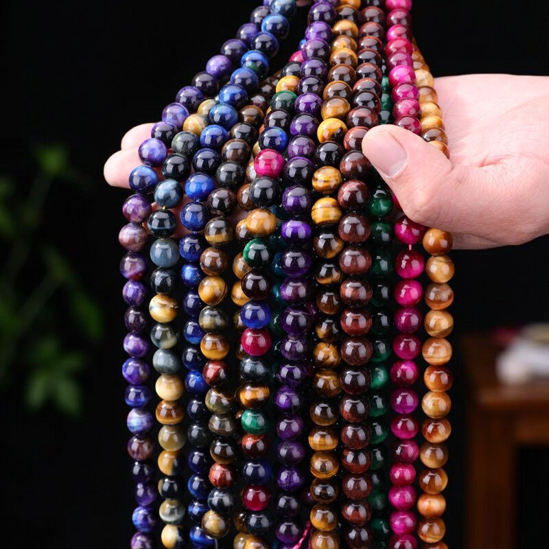 Hand holding several strands of colorful round tiger eye beads