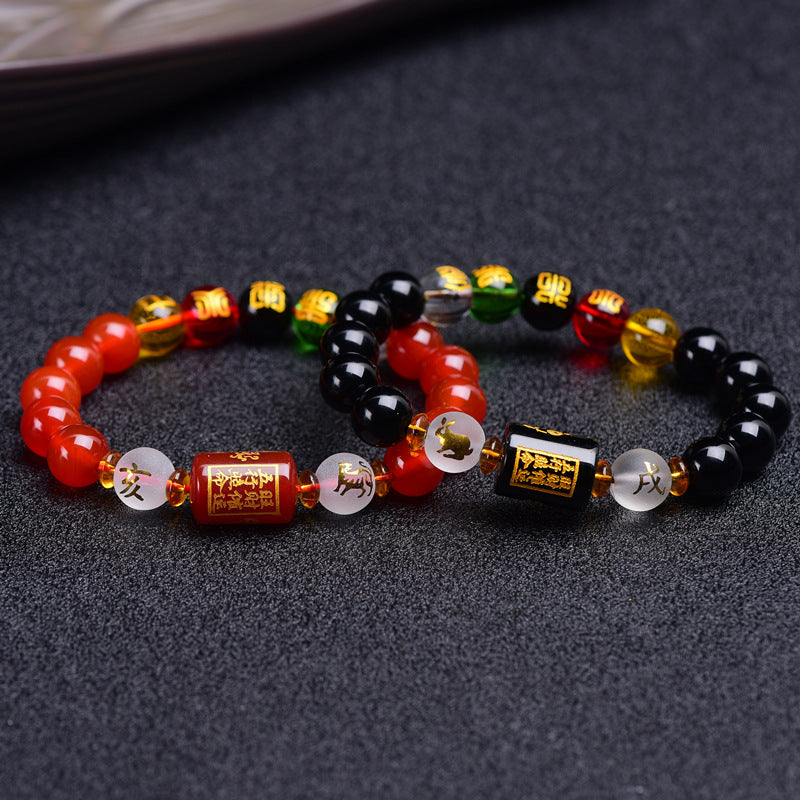 Red agate and black obsidian bracelets with gold-tone zodiac charms on a dark surface