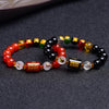 Red agate and black obsidian bracelets with gold-tone zodiac charms on a dark surface
