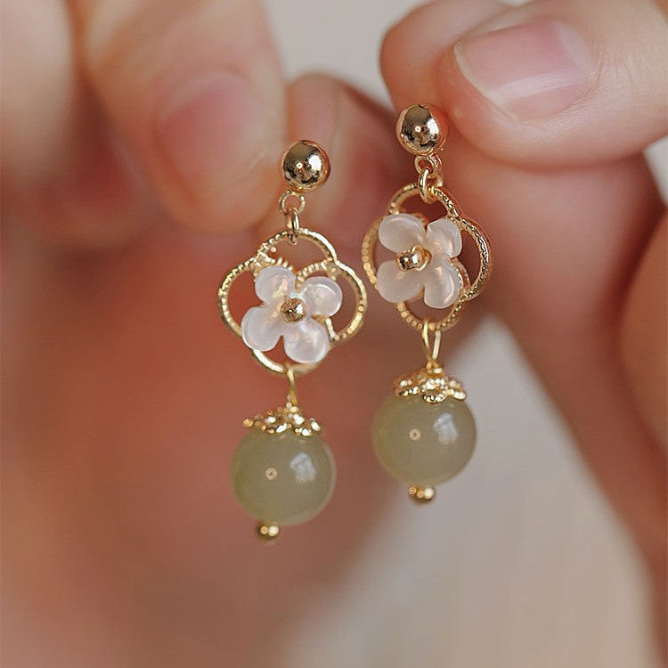 Close-up of gold-tone earrings with white shell flowers and green jade beads