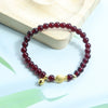 Close-up of a handwoven garnet bead bracelet with a gold-tone gourd charm on a wooden surface