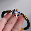 Close-up of a hand holding a black braided bracelet with a colorful enamel lion head charm
