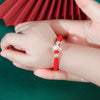 Child wearing a red rope bracelet with a silver zodiac animal charm