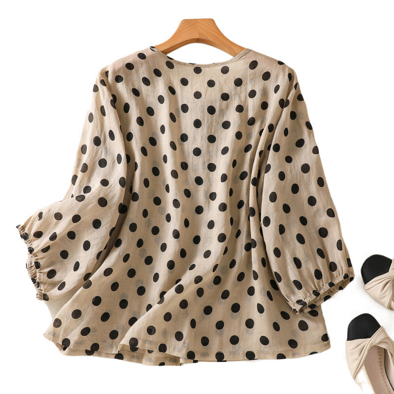 Beige women's blouse with black polka dots hanging on a wooden hanger