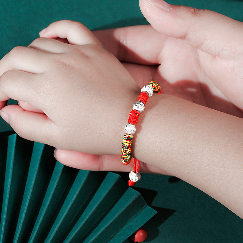 Child wearing a handmade red string bracelet with silver beads and a dragon knot.
