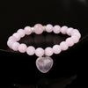 Pink rose quartz beaded bracelet with a heart charm on a black background