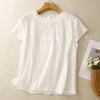 White women's short sleeve shirt with ruffled neckline and pleated chest detail hanging on a wooden hanger