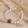 Gold-tone bracelet with white freshwater pearls and a single red agate bead on beige fabric