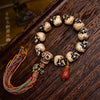 Close up of a camel bone bracelet with carved skull beads and a colorful tassel on a wooden surface