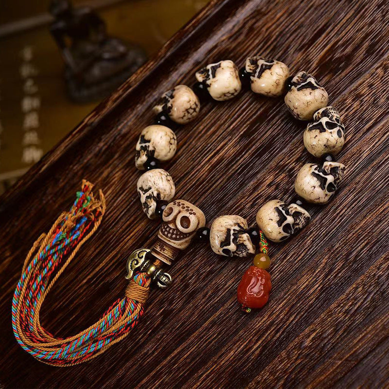 Close up of a camel bone bracelet with carved skull beads and a colorful tassel on a wooden surface