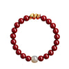 Red cinnabar beaded bracelet with a gold snake charm and one white accent bead on a white background