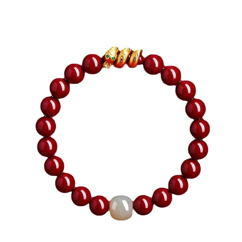 Red cinnabar beaded bracelet with a gold snake charm and one white accent bead on a white background