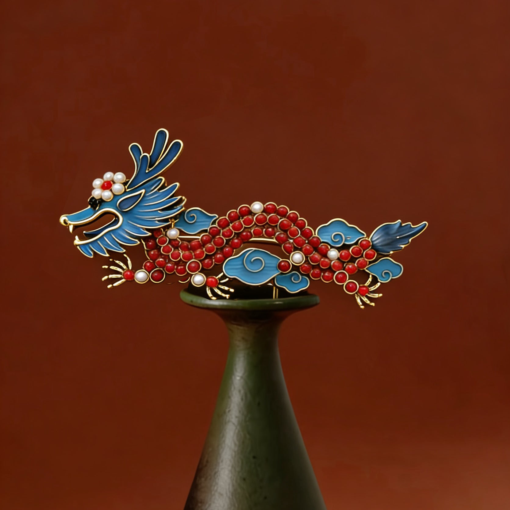 Close up of a red and blue enamel dragon brooch on a stand