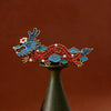 Close up of a red and blue enamel dragon brooch on a stand