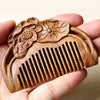 Hand holding a small sandalwood comb with carved lotus flowers