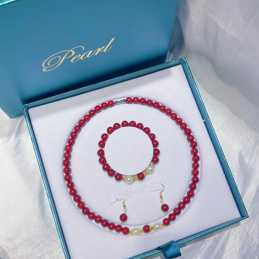 Three-piece jewelry set with red cinnabar beads and white shell beads in a blue box