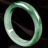 Close up view of a translucent green jade bangle bracelet on a dark background