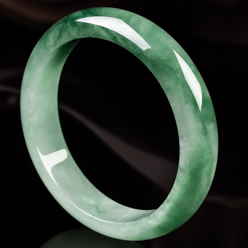Close up view of a translucent green jade bangle bracelet on a dark background