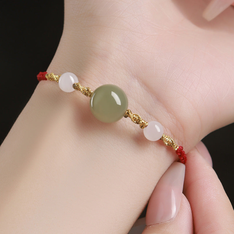 Close-up of a hand wearing a red braided bracelet with a green jade bead