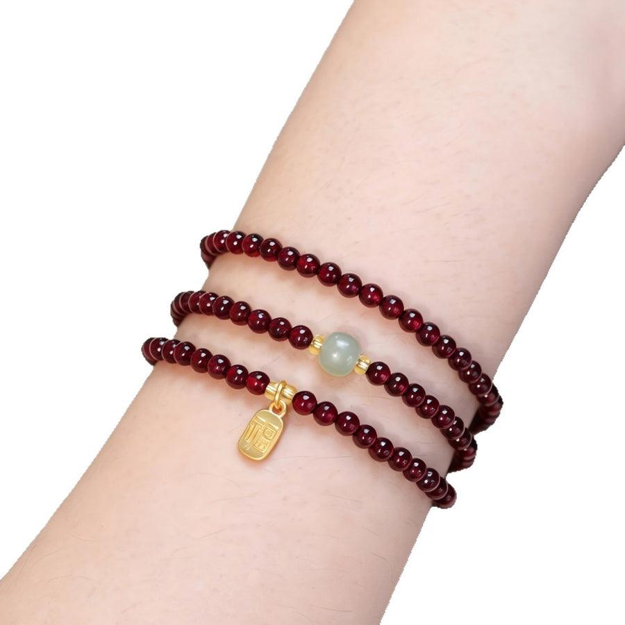 Close up of a triple wrap garnet bracelet with a gold tone fu charm on a wrist